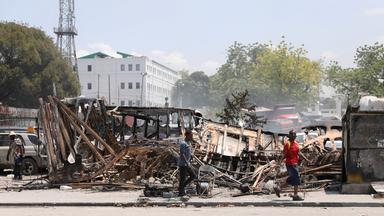 In Port-au-Prince, Haiti, gehen Menschen an Fahrzeugüberresten vorbei, nachdem sie von Banden in Brand gesteckt wurden (Archivbild 23. März 2024).