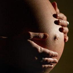 Eine hochschwangere Frau umfasst ihren Bauch mit beiden Händen.
