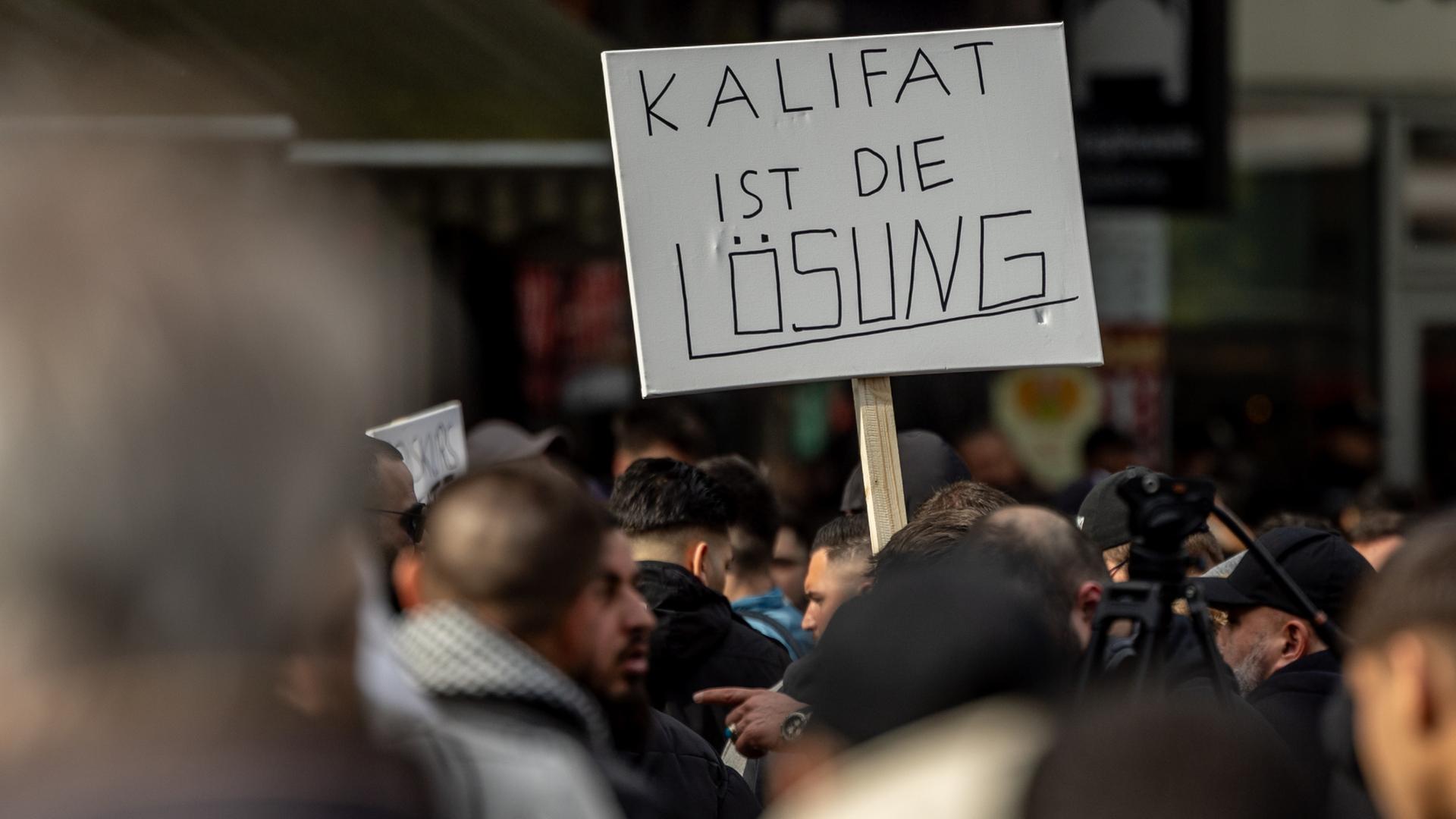 Teilnehmer einer Islamisten-Demonstration in Hamburg halten ein Plakat mit der Aufschrift "Kalifat ist die Lösung" in die Höhe.