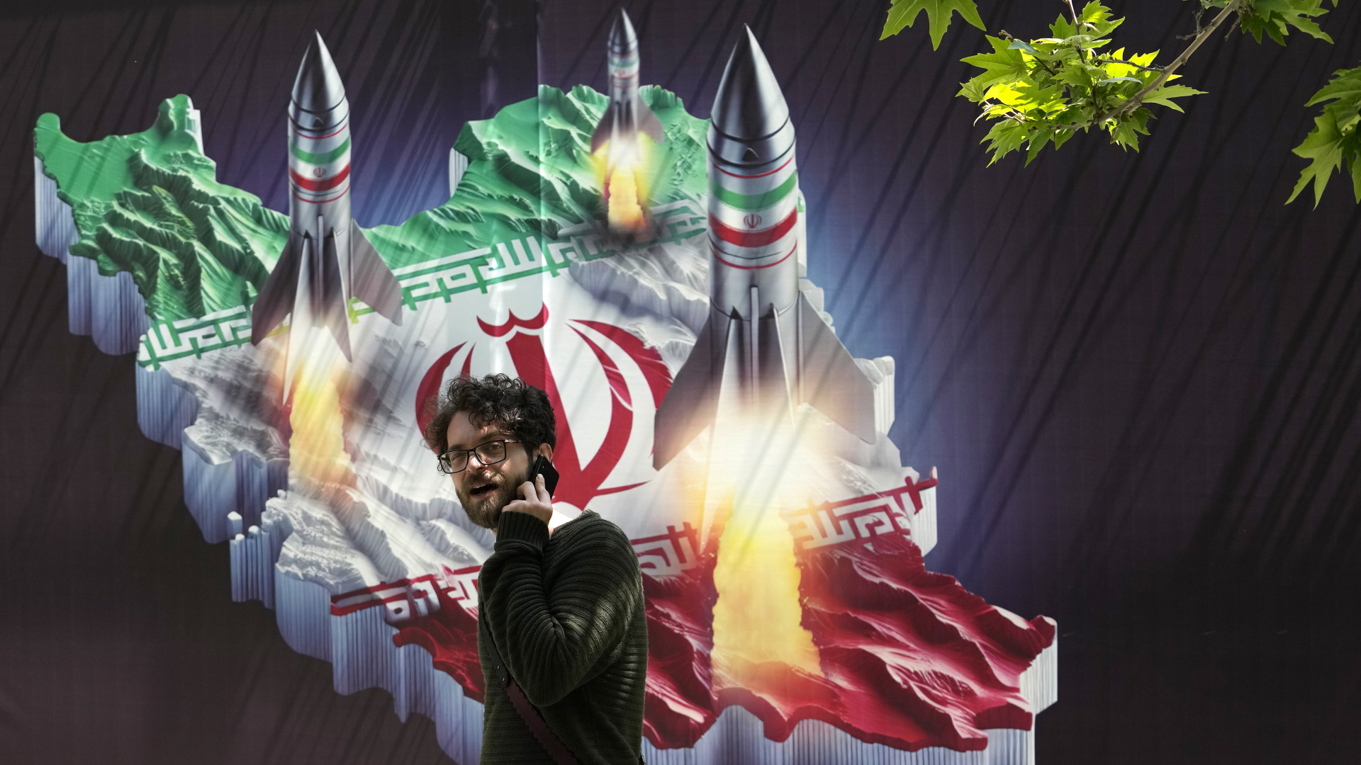 Ein Passant, der mit einem Handy telefoniert, geht in Teheran an einem Banner vorbei, das den Abschuss von Raketen von der iranischen Landkarte zeigt. 