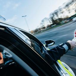 Ein Polizist hält eine rote Polizeikelle aus dem Beifahrerfenster eines Streifenwagens heraus. 