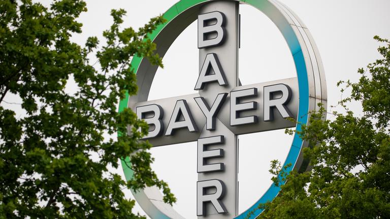 Das Bayer Kreuz, Logo des Unternehmens Bayer, steht zwischen Bäumen am Flughafen Köln/Bonn.