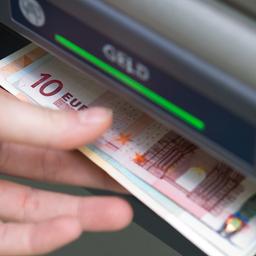 Eine Hand greift nach Geldscheinen, die aus einem Geldautomaten ausgeworfen wurden