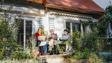 Eine Familie sitzt vor einem Haus auf einer Terrasse.