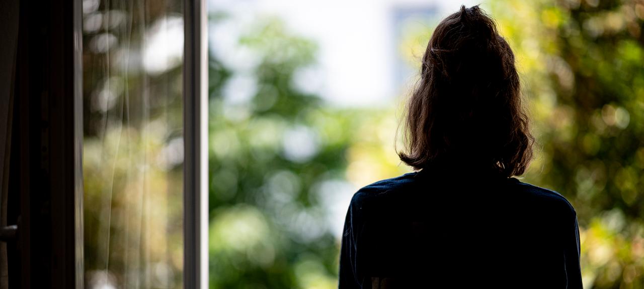 Eine Frau steht in ihrer Wohnung an einem Fenster.