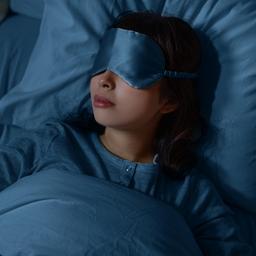 Eine Frau schläft nachts zu Hause im Bett mit Schlafmaske.