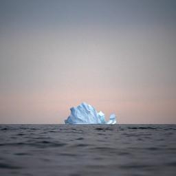 Ein Eisberg schwimmt vor Grönland bei Sonnenuntergang auf dem Meer.