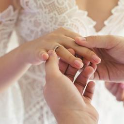 Ein Bräutigam steckt seiner Braut den Ehering an den Ringfinger.