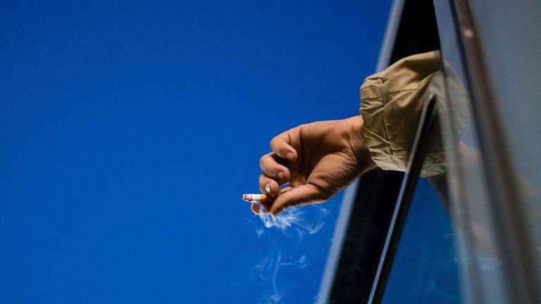 Eine brennende Zigarette wird aus einem Fenster gehalten.