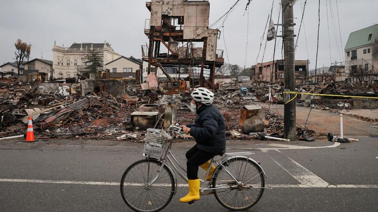 Eine Japanerin fährt mit dem Fahrrad durch die durch ein Erdbeben zerstörte Region Ishikawa.