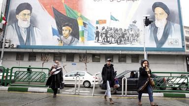 Menschen gehen in der Innenstadt von Teheran unter einem riesigen Wandgemälde von Ayatollah Ruhollah Khomeini (r.) und Ayatollah Ali Khamenei (l.) entlang.