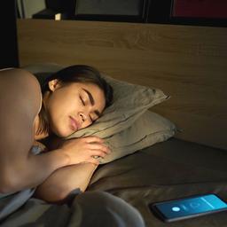 Eine schlafende Frau, neben ihr liegt ein Mobiltelefon im Bett