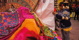 A local woman sells patterned fabrics in electric pink and blue, orange, green and red, at Cusco's lively Baratillo market.