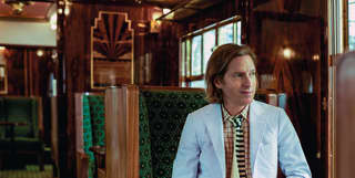 Filmmaker Wes Anderson sits at a French polished table in an art deco carriage and observes the world through the window