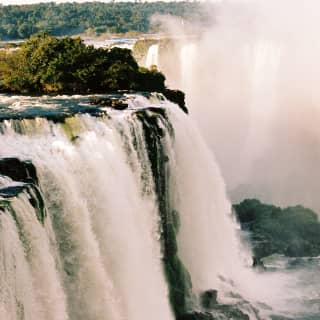 Dramatic shot of Iguassu Falls as white water thunders over the rocky brink and clouds of mist and spray dance in the air.