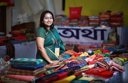 Smiling woman selling bright-colored textiles at a market.