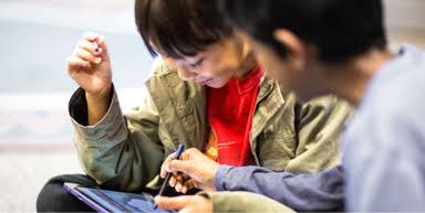 有兩個孩童在玩平板電腦，其中一位在教另一位如何使用裝置。