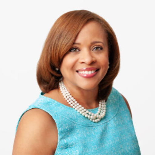 Portrait of a smiling Black woman with short auburn hair, wearing a pearl necklace and a light blue dress