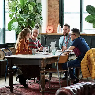 Vier Arbeitskolleg*innen sitzen an einem Besprechungstisch in einem hübschen Büroraum mit Grünpflanzen.