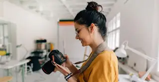 Uma mulher sorri enquanto usa uma câmara DSLR.