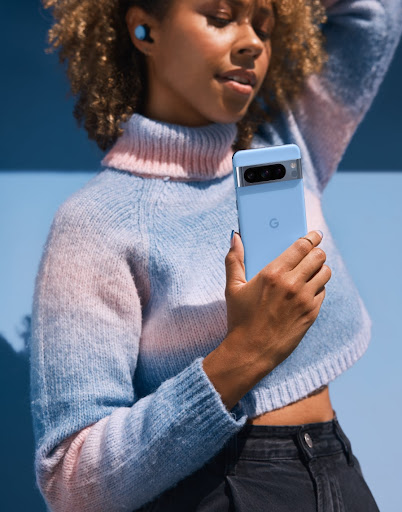 Eine Person hält ihr Pixel Smartphone in der Farbe Bay in der Hand. Sie steht vor einem Hintergrund mit derselben Farbe.