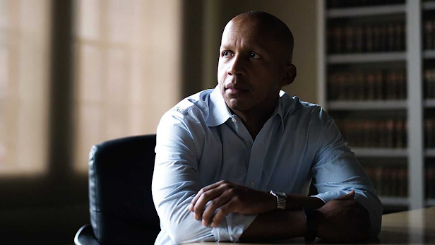 Black man in a dress shirt sitting at a desk with his arms crossed