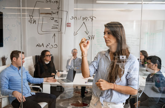 Group of people in a conference room with woman in front writing on board.