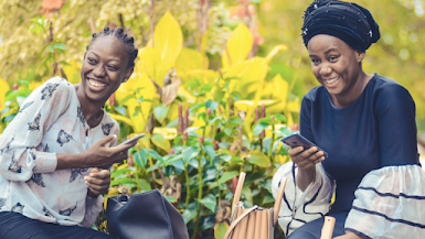 Two black women in colorful dresses hold smartphones and smile