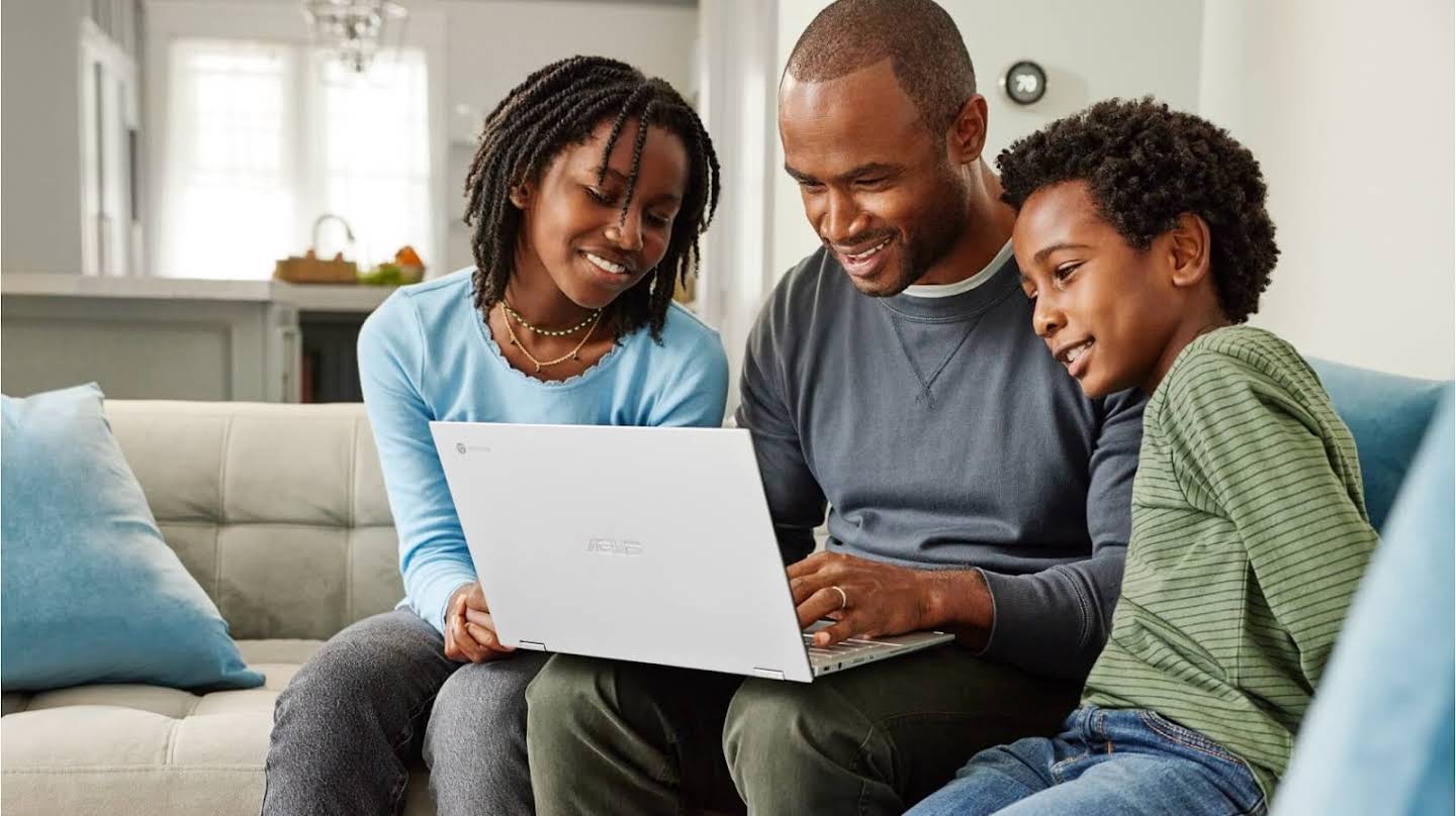 Man aan het werk op een Chromebook thuis met twee kinderen die samen naar het scherm kijken.