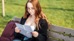 Young student girl in glasses and with laptop and books reading letter outdoors