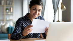 Woman smiling at letter in front of laptop.