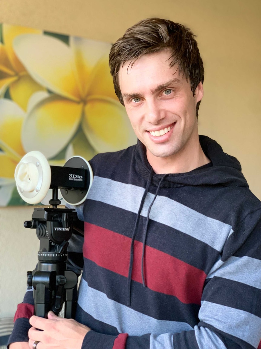A young man smiling and holding a camera