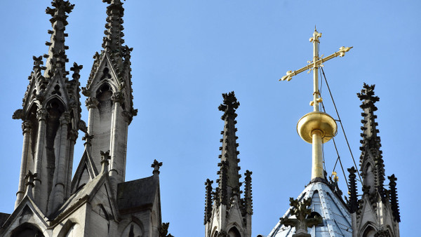 Ein goldenes Kreuz auf dem Kölner Dom leuchtet in der Sonne.