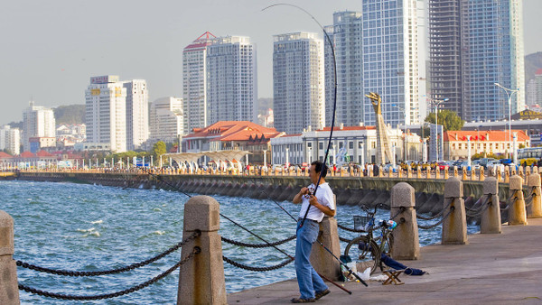Ein Mann fischt am Rande der Skyline von Yantai.