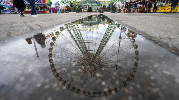 Ein Riesenrad spiegelt sich in einer Pfütze auf dem Festgelände des Stuttgarter Frühlingsfestes.