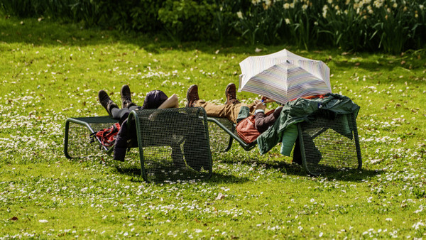 Besucher Sonnen sich Ende März im Frankfurter Palmengarten auf einer Liegewiese.