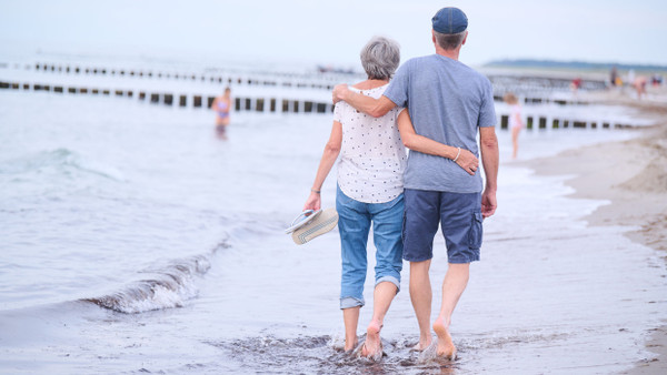 Ein Rentnerehepaar geht am Strand Arm in Arm spazieren. (Symbolbild)