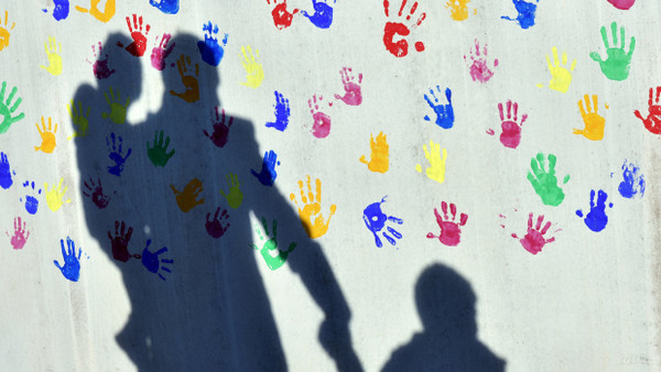 Vor einer Kita in München: Ein Mann mit Kind auf dem Arm wirft einen Schatten auf eine Wand.