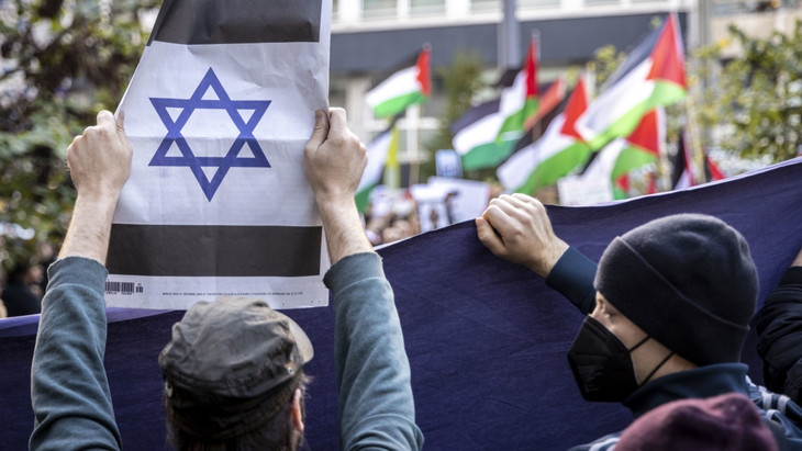 Ein proisraelischer Gegendemonstrant zeigt in Düsseldorf eine jüdische Zeitung mit einem Davidstern, im Hintergrund propalästinensische Demonstranten.