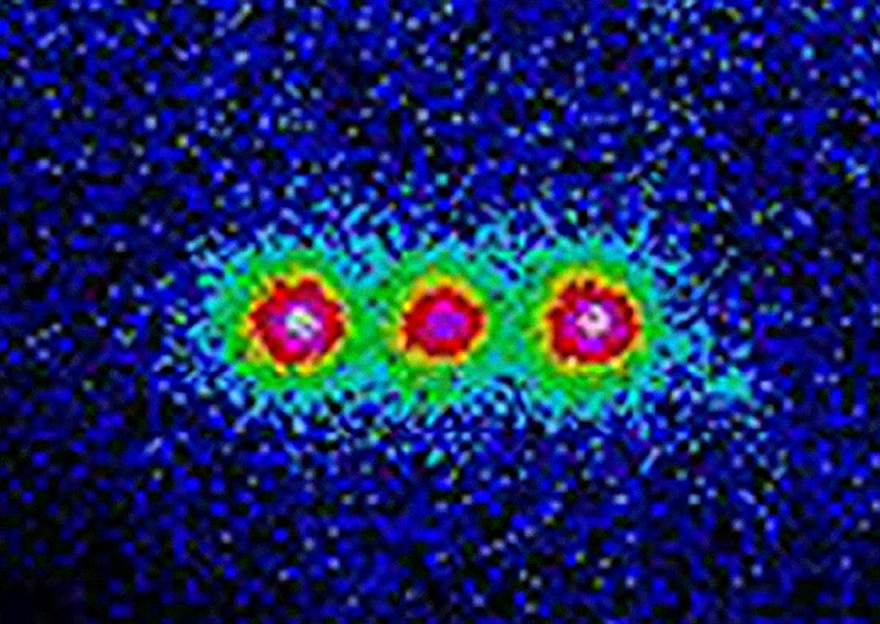Drei fluoreszierende Berylliumionen, gefangen und quantenmechanisch verschränkt in einer Teilchenfalle. Ändert ein Ion seinen Zustand, dann spüren das sofort seine Nachbarn.