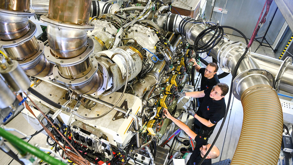Ein Techniker und zwei Ingenieure arbeiten in einem MTU-Prüfstand an einem mobilen MTU-Gasmotor von Rolls-Royce.
