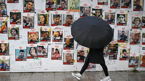 A person with an umbrella walks in Tel Aviv in the rain past banners displaying photos of hostages kidnapped by Hamas, February 19, 2024.