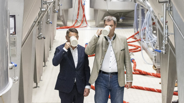 Markus Söder, und Boris Rhein trinken bei einem Besuch in der Brauerei Glaabsbräu zwischen den Kesseln ein Bier, aufgenommen am 21. August 2023 in Seligenstadt.
