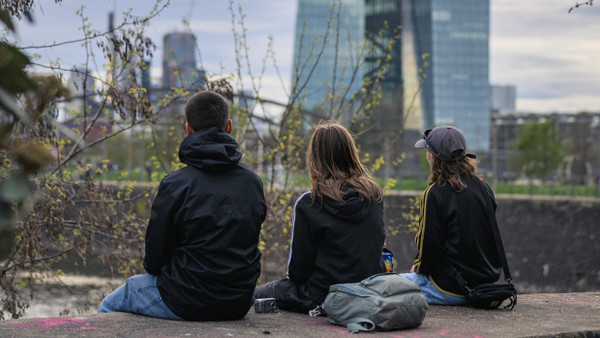 Jugendliche sitzen am Frankfurter Mainufer mit Blick auf die Europäische Zentralbank.