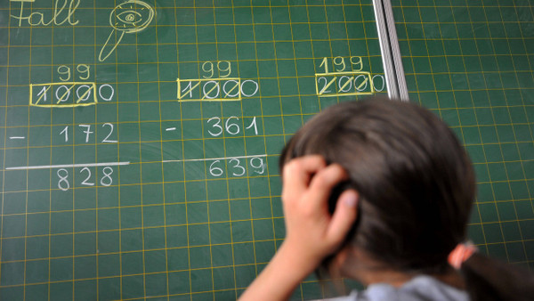 Ein Mädchen der zweiten Klasse einer Grundschule in München steht an der Tafel vor einer Rechenaufgabe.