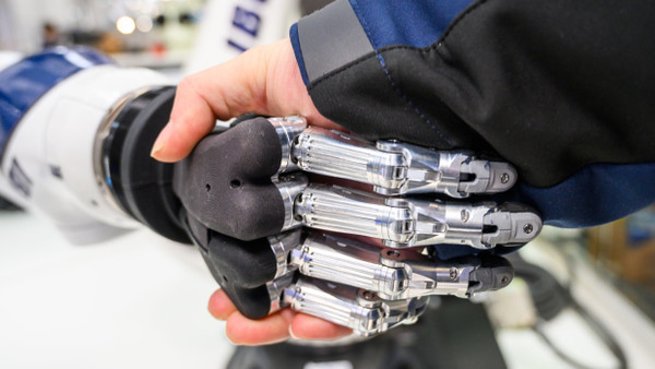 An einem Stand auf der Hannover Messe 2019 gibt ein Mann einem Roboter die Hand.