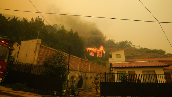 Ein Feuerwehrmann rennt durch einen Vorgarten in dem chilenischen Ort Vina del Mar, während ein Gebäude in Flammen aufgeht.