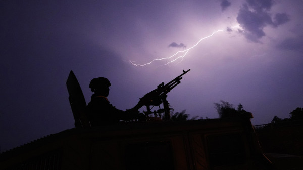 Blitze erhellen den Himmel während ein Schütze auf gepanzerten thailändischen Militärfahrzeugs nahe des Moei-Flusses Wache hält.