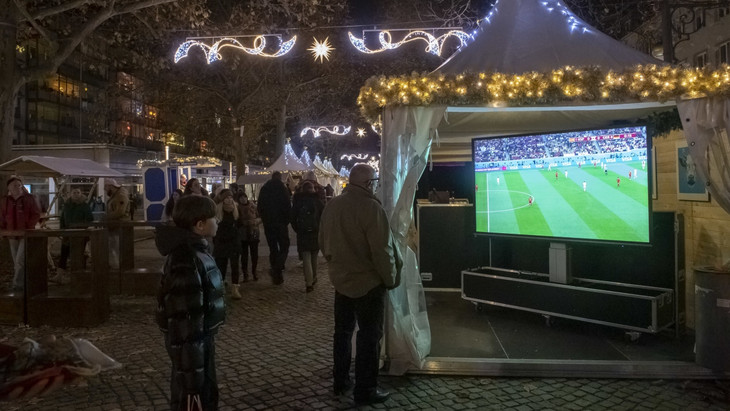 Weihnachtsmarktbesucher schauen in Dresden das WM-Spiel Deutschland gegen Spanien.