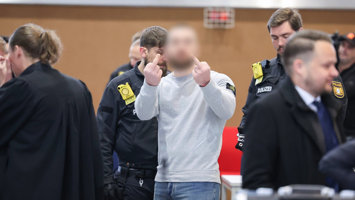 Während des Prozessbeginns gegen die beiden Geldautomaten-Sprenger-Banden in Bamberg zeigt einer der Angeklagten seine beiden Mittelfinger in die Kamera.